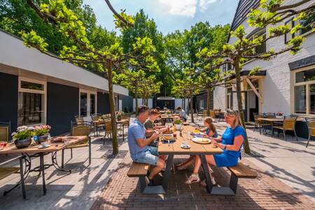 Die Familie isst auf der Terrasse des Restaurants im Ferienpark EuroParcs De Hooge Veluwe