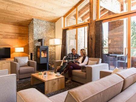 2 Personen im Wohnzimmer mit Holzofen einer Wohnung in der Landal Alpine Lodge Lenzerheide