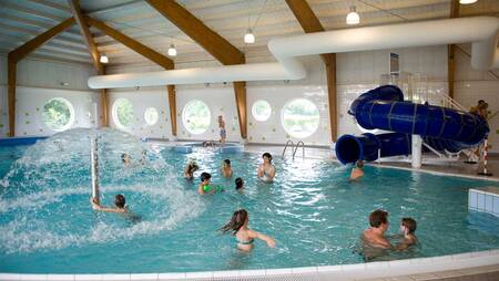 Menschen schwimmen im Hallenbad mit Rutsche im Ferienpark Molecaten Park Flevostrand