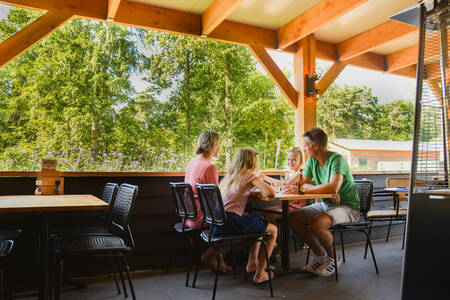Familie isst auf der überdachten Terrasse des Restaurants im Ferienpark RCN De Noordster