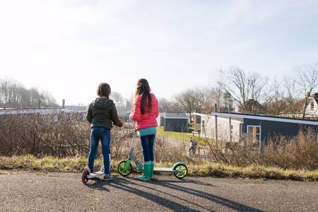 2 Kinder auf Rollern vor Chalets im Ferienpark RCN Toppershoedje