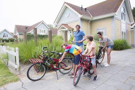 Familie mit Fahrrädern vor einem Ferienhaus im Roompot Noordzee Résidence De Banjaard