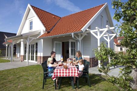 Die Familie isst an einem Tisch im Garten eines Ferienhauses in der Roompot Résidence Klein Vink